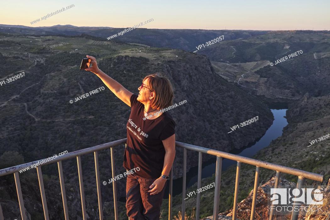 Stock Photo: A middle-aged woman takes a selfie with her mobile phone in the viewpoint next to the hermitage of Nuestra Señora del Castillo and from which the Duero River.
