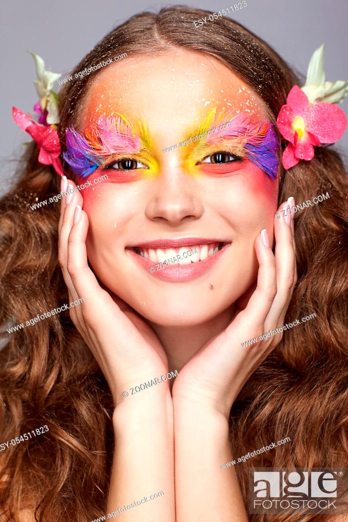 Stock Photo: Portrait of happy smiling teen girl with hands near face. Young female with unusual stylish make-up and false fashion feather eyelashes.
