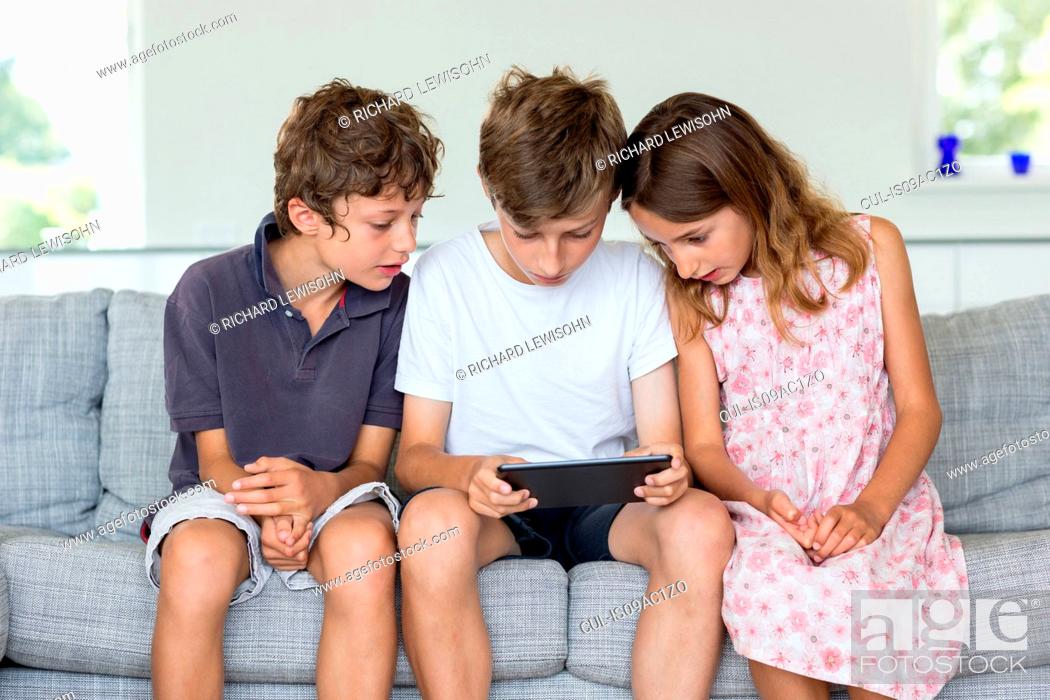 Stock Photo: Brothers and sister on sofa looking at digital tablet.