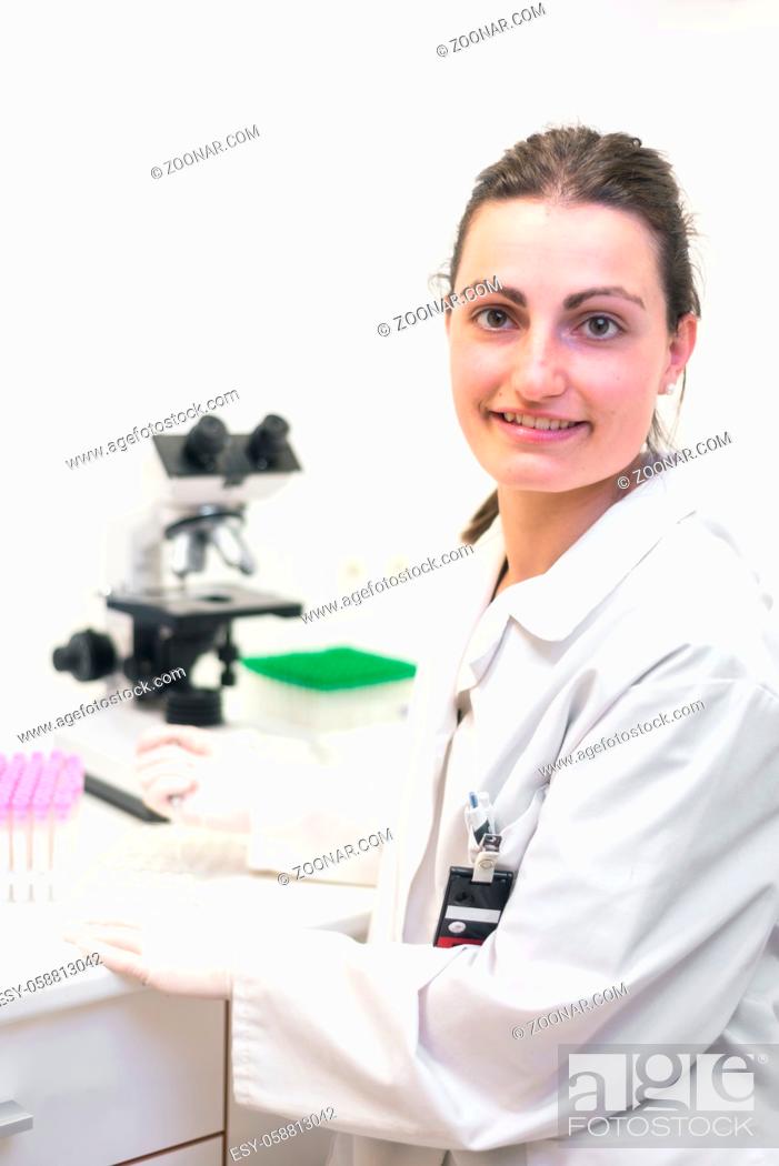 Photo de stock: Female researcher smiling. Female researcher using microscope and smiling at camera in the laboratory .