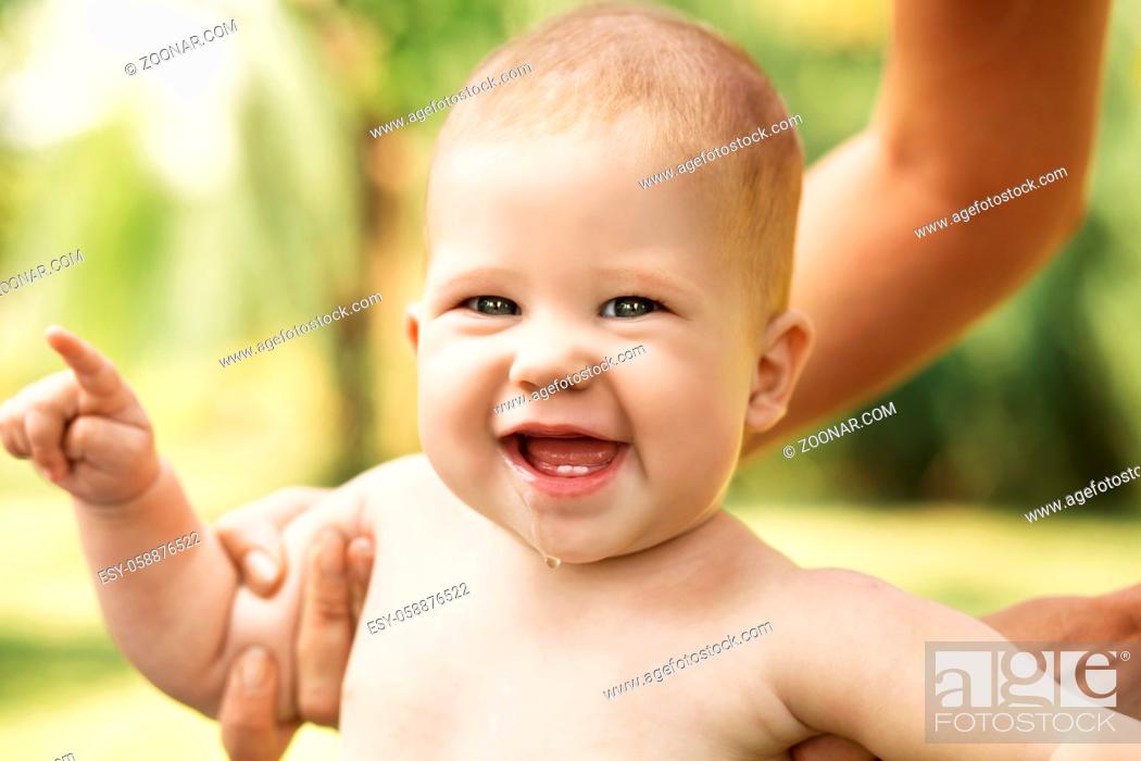 Imagen: Portrait of a beautiful baby holding the mother's hand against green nature background outdoors.