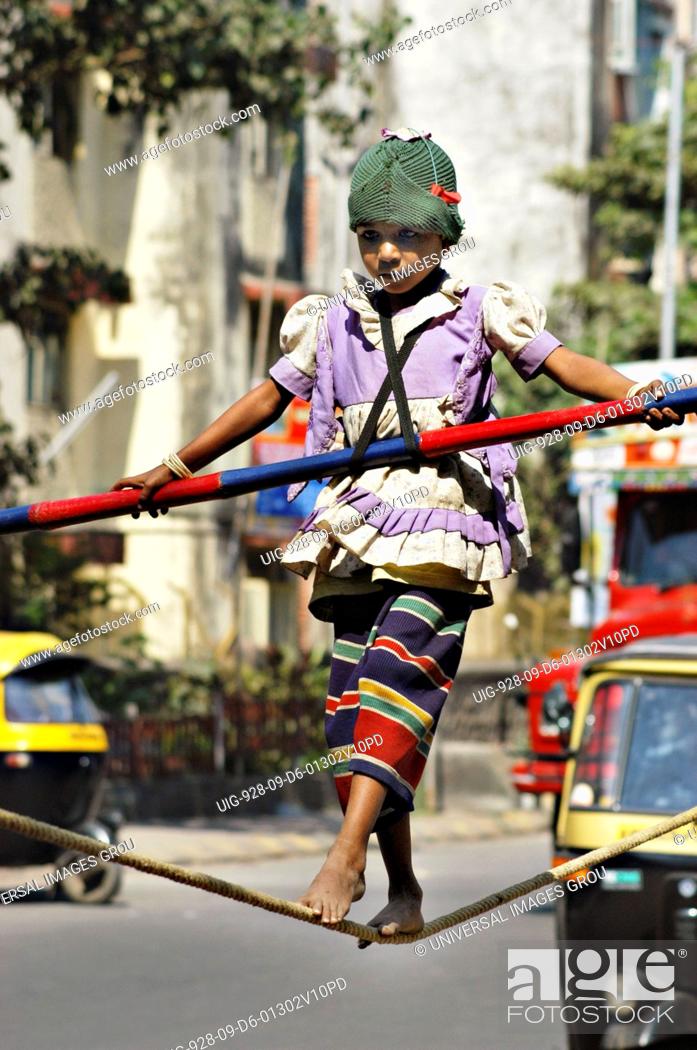 Stock Photo: South Asian Girl Working Street Performer Balancing Act By Walking On Rope With Bamboo In Hand.