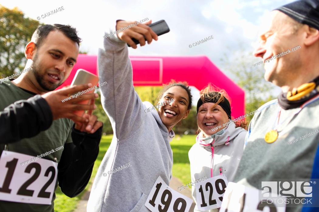 Photo de stock: Happy runner friends taking selfie with camera phone at charity run in park.