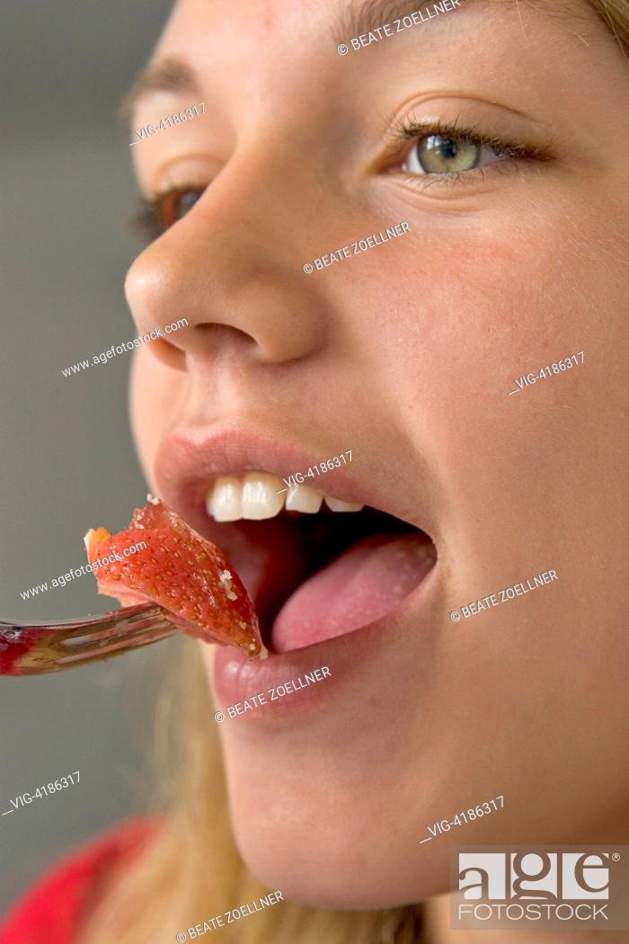 Stock Photo: Close-up : girl opens her mouth and puts a piece of strawberry with a - , , Germany, 17/06/2006.