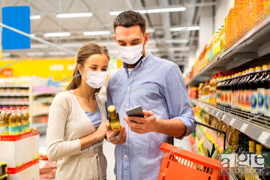 Stock Photo: couple in masks with phone and olive oil at store.