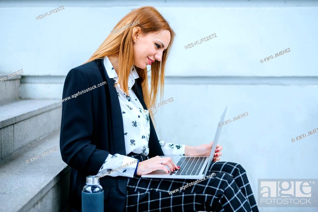 Stock Photo: Young businesswoman sitting on stairs using laptop.