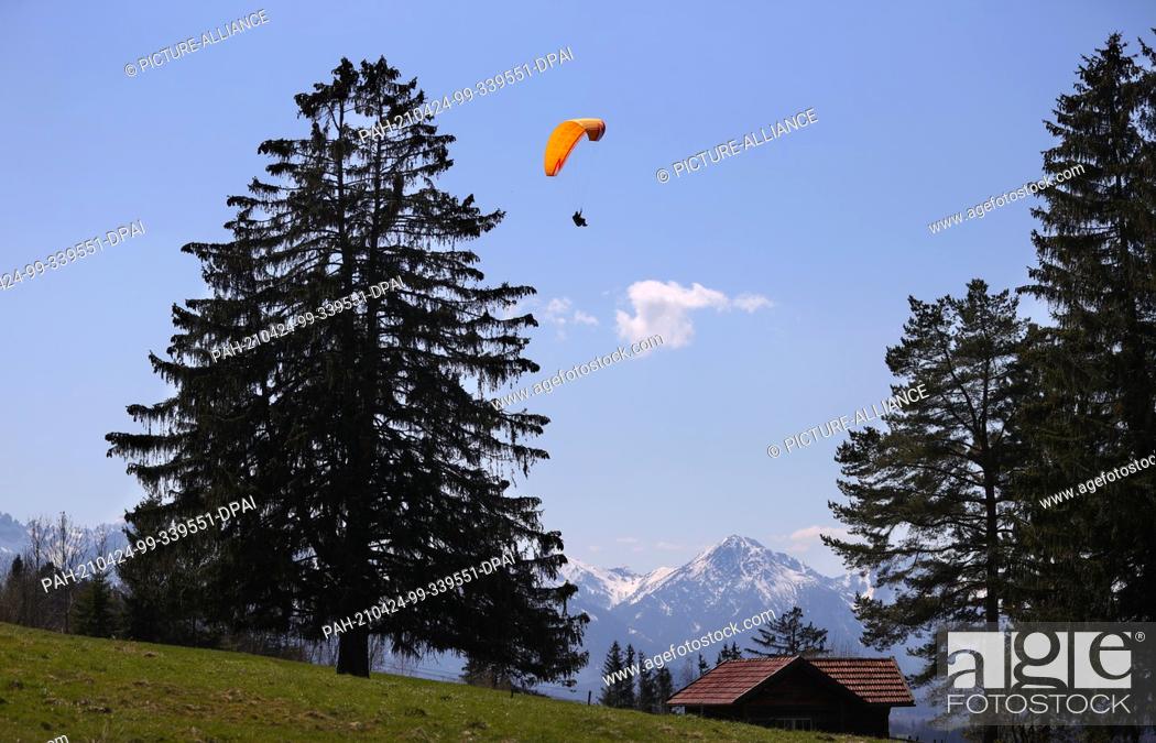 Stock Photo: 24 April 2021, Bavaria, Buching: A paraglider glides over a mountain meadow on the Buchenberg. Photo: Karl-Josef Hildenbrand/dpa.