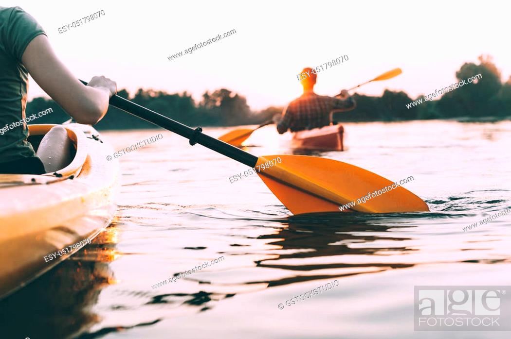 Stock Photo: People kayaking. Rear view cropped image of people kayaking on river with sunset in the background.