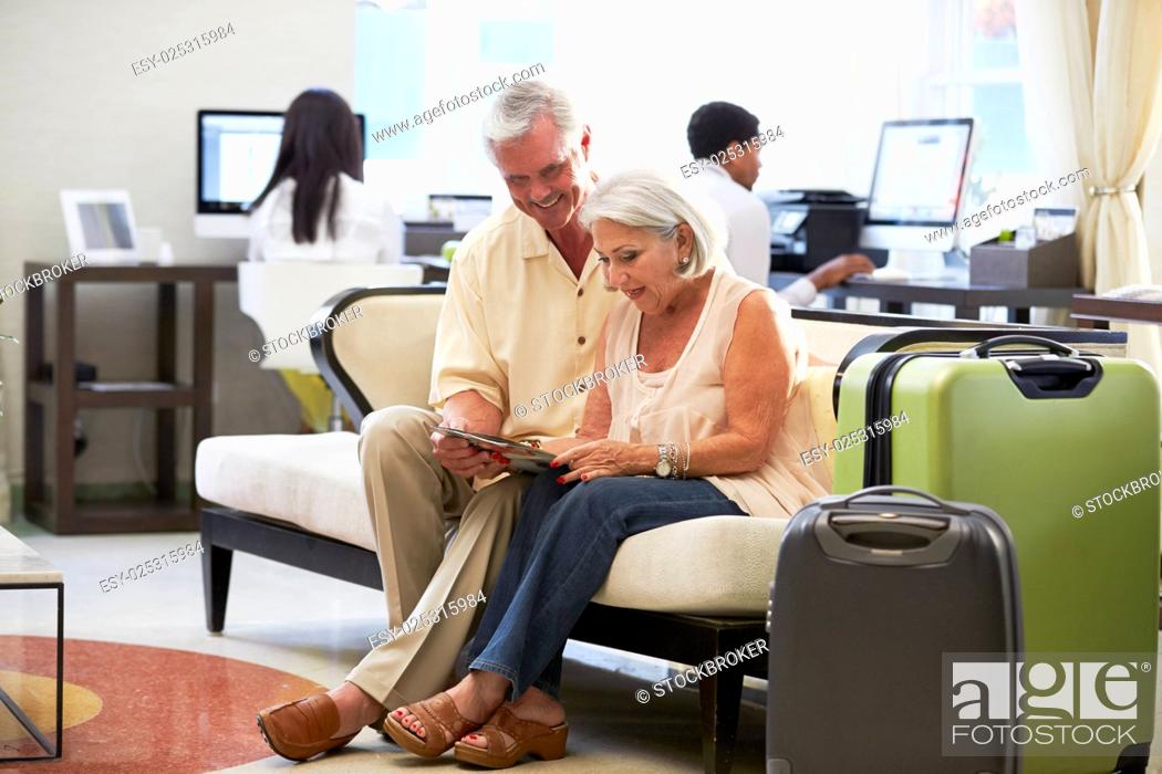Stock Photo: Senior Couple In Hotel Lobby Looking At Digital Tablet.