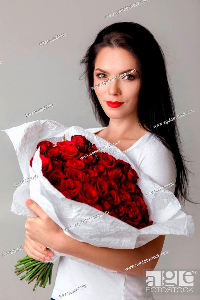 Stock Photo: beautiful smiling young woman holding large bouquet of red roses on gray background.
