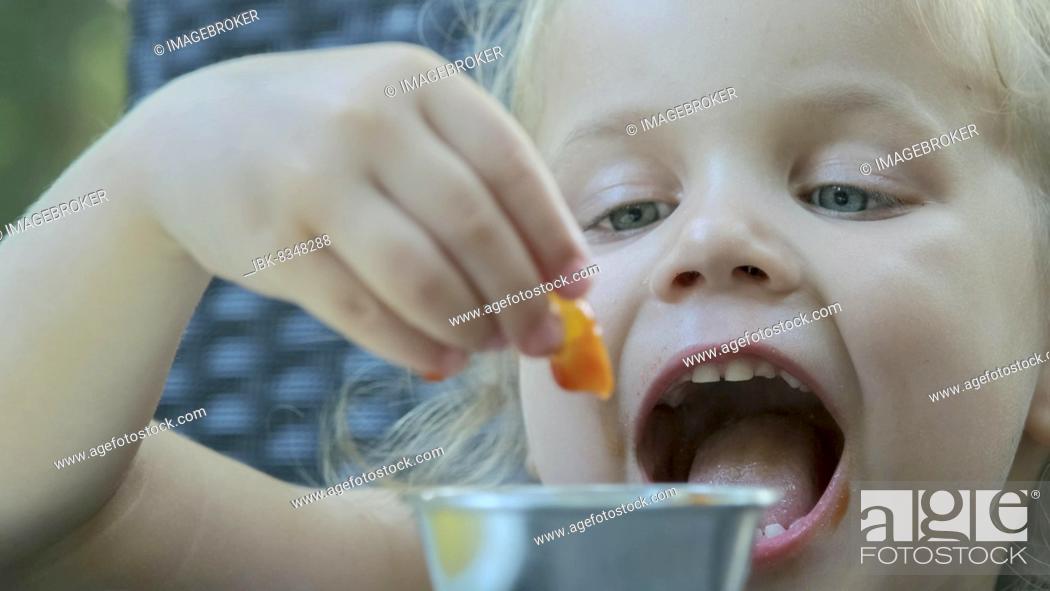 Stock Photo: Little girl eat french fries. Close-up of blonde girl takes potato chips with her hands and tries them sitting in street cafe on the park.