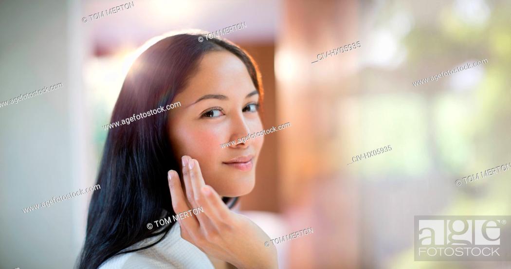 Stock Photo: Portrait confident young woman applying moisturizer to face.