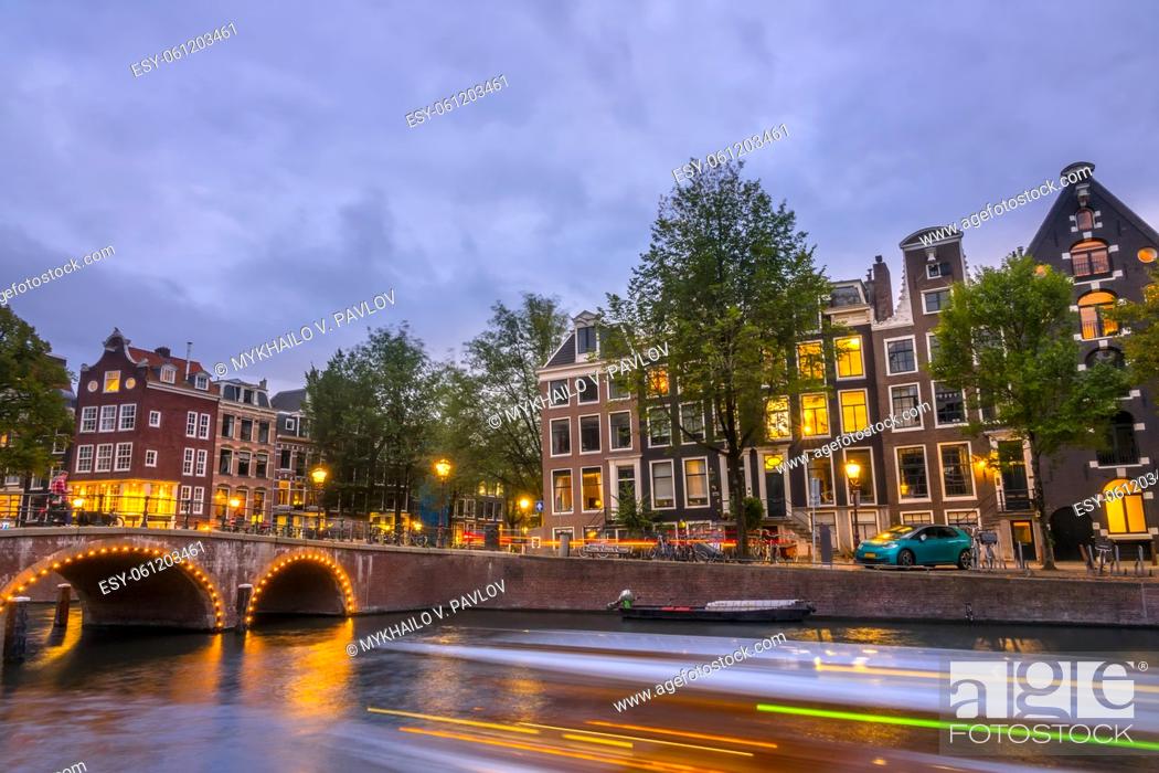 Stock Photo: Netherlands. Evening on the Amsterdam canal. Old stone bridge and typical houses on the embankment. Traffic on the water and streets.