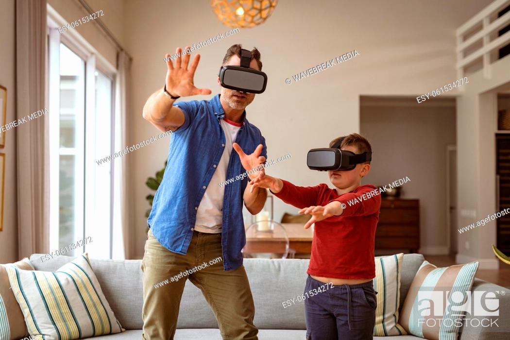 Stock Photo: Caucasian father and son wearing vr headsets gesturing while standing in the living room at home.