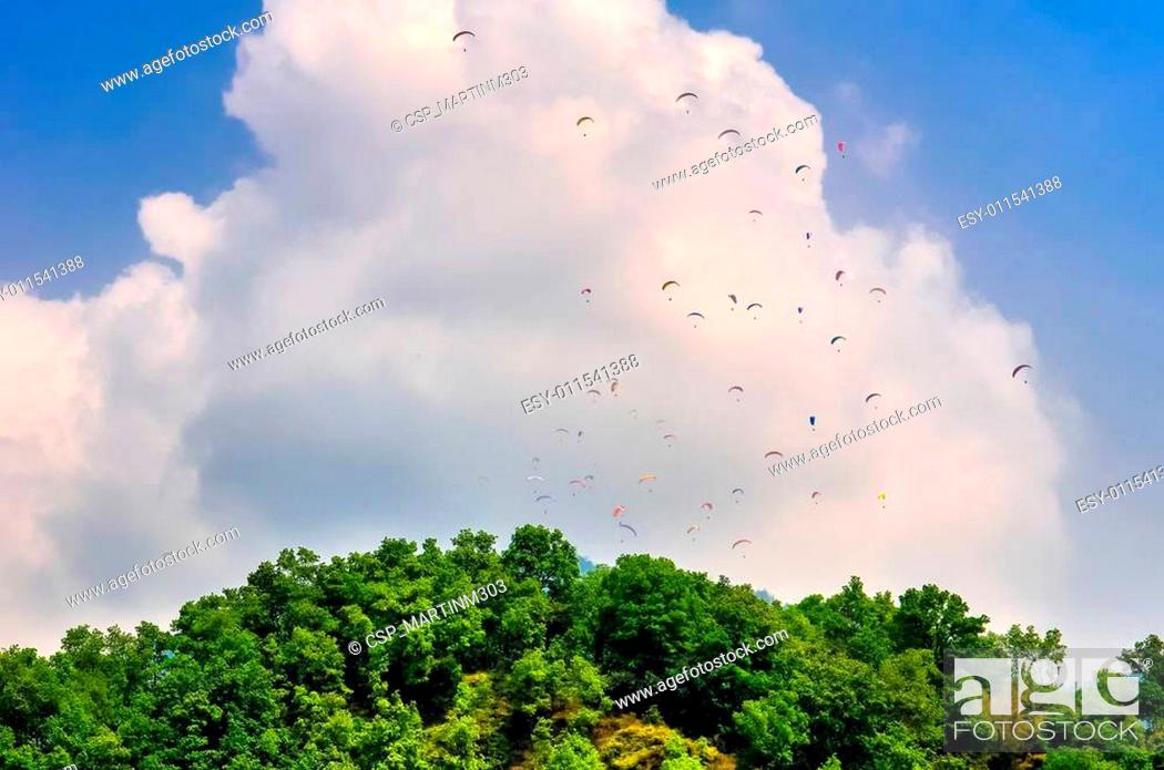 Stock Photo: Many parachutists paragliding above green mountain.