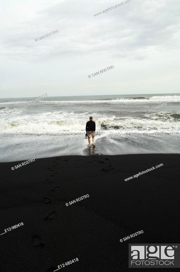 Stock Photo: Iceland, Vik village, church, man with feet in the sea at the black sand beach.