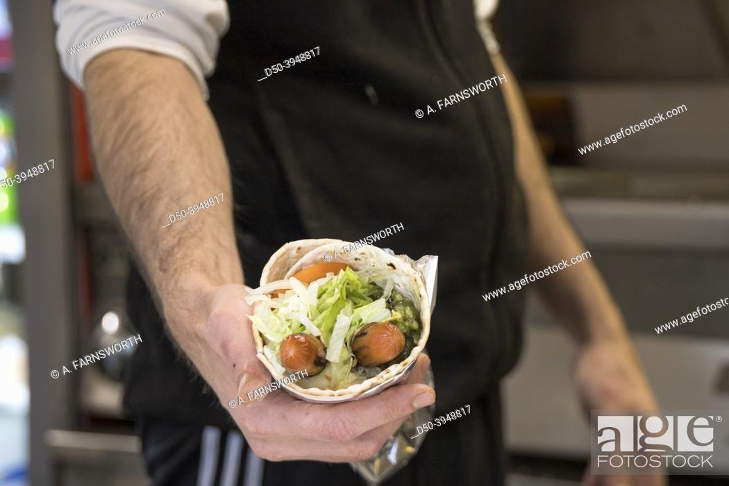 Stock Photo: A classic Swedish tunnbrodsrulle, a wrap with mashed potaoes, hotdogs, salad and a condiment like pickled cucumbers, held by a fast food cook.