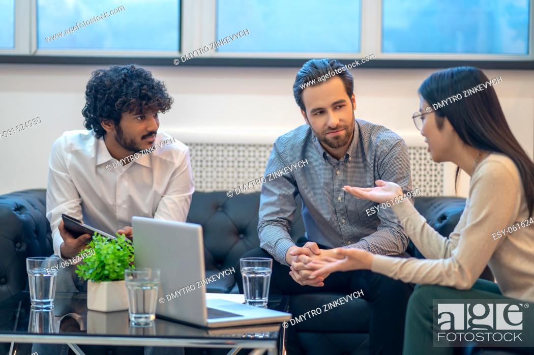 Stock Photo: Focused young company workers sitting at the coffee table and listening to their female colleague.