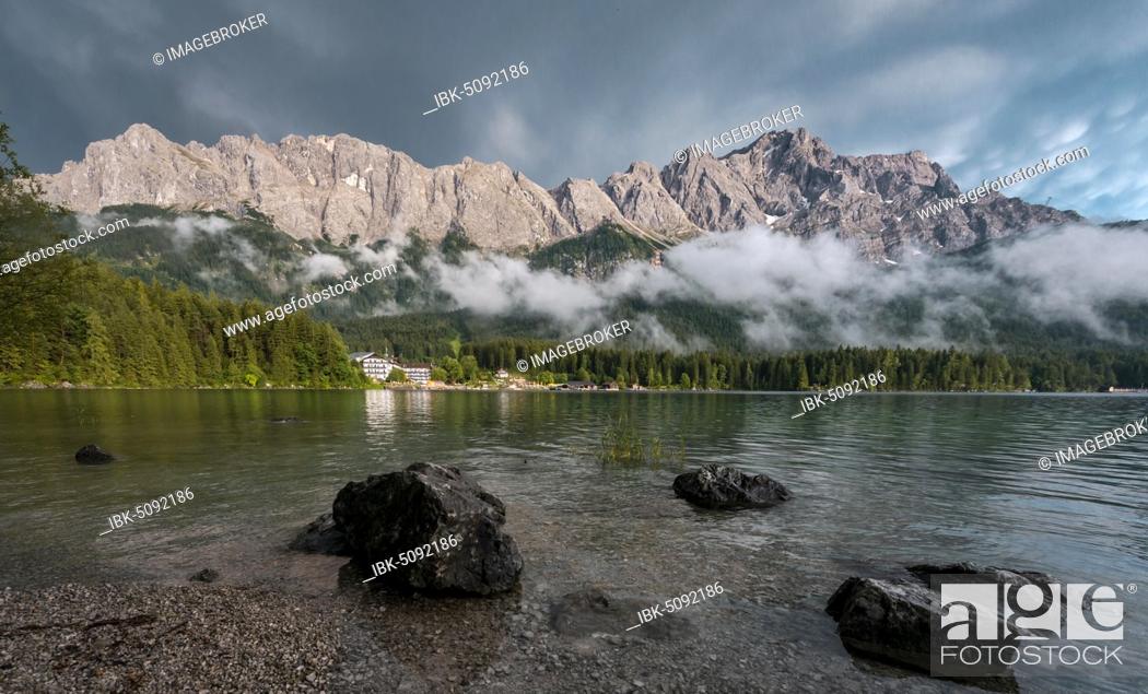 Imagen: Rocks on the shore, Eibsee lake in front of Zugspitze massif with Zugspitze, low hanging clouds, Wetterstein range, near Grainau, Upper Bavaria, Bavaria.