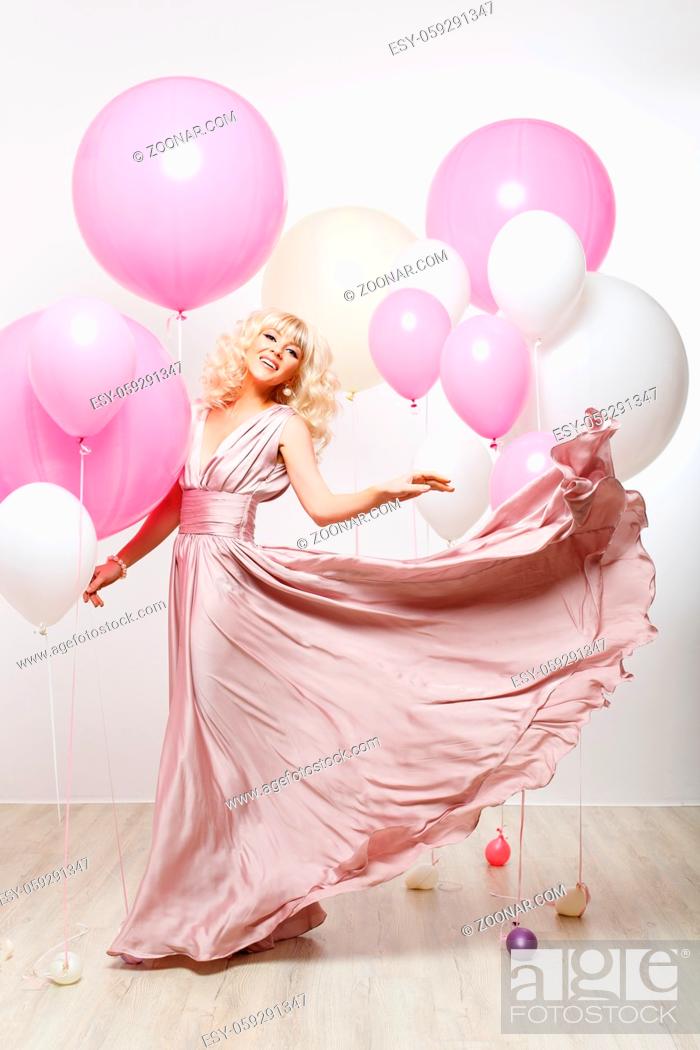 Stock Photo: beautiful blonde young cheerful woman in long pink dress holding many air balloons. studio shot over white background. copy space.