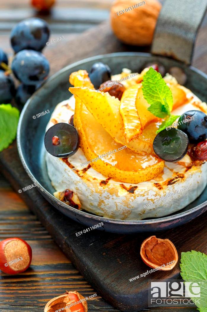 Stock Photo: Grilled camembert with pears and black grapes in a cast iron pan on a wooden stand, selective focus.
