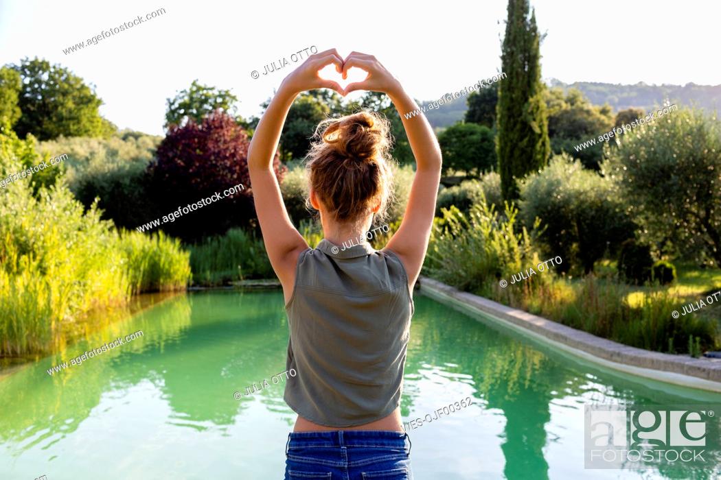 Stock Photo: Rear view of a girl standing at swimming pool, forming a heart with her hands.