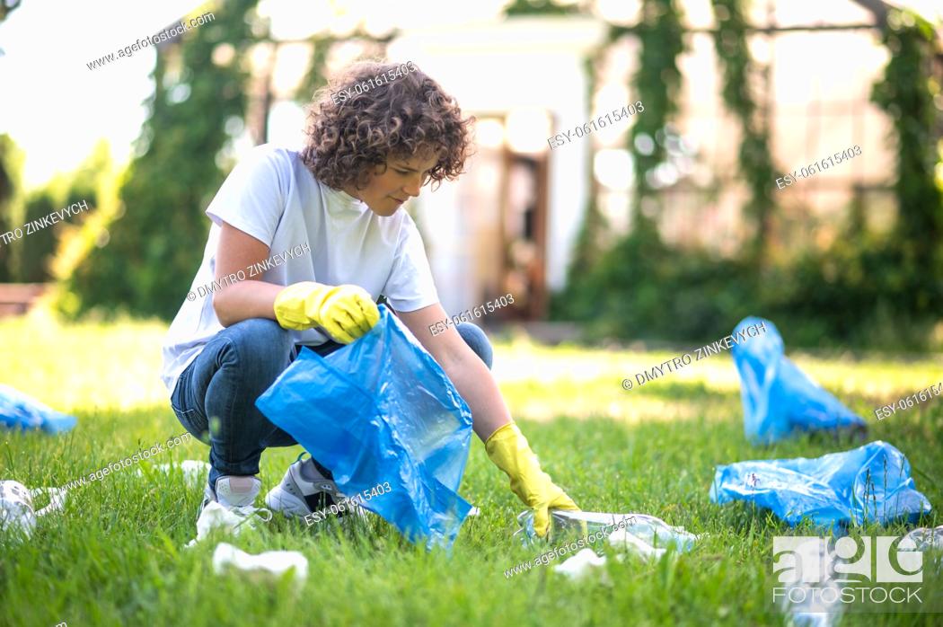 Stock Photo: Gathering garbage. Curly-haired teen gathering garbage in the park.
