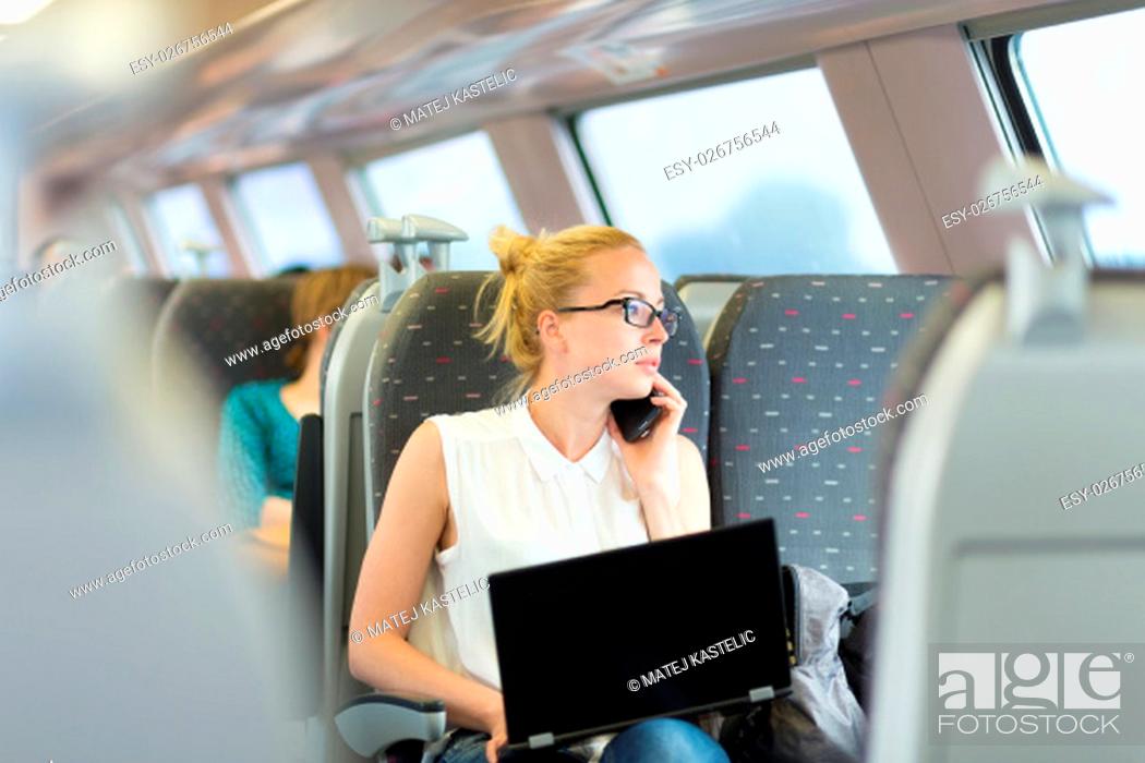 Stock Photo: Businesswoman talking on cellphone and working on laptop while traveling by train. Business travel concept.