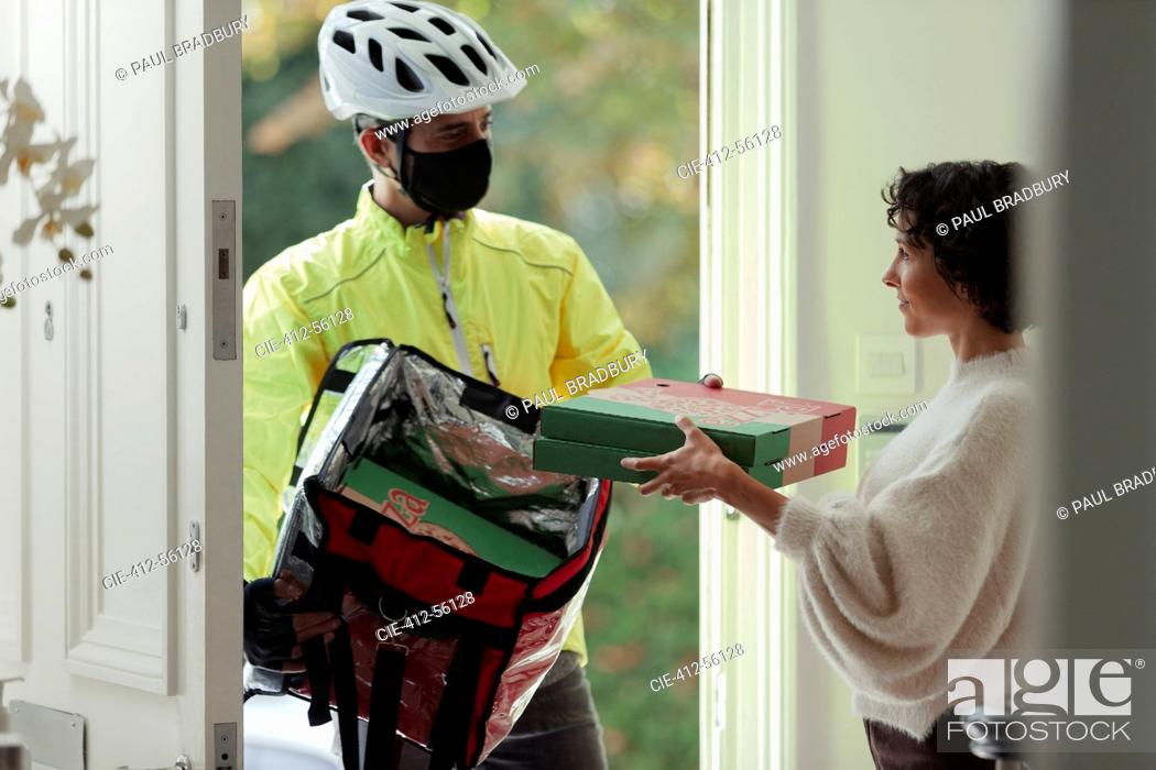 Imagen: Woman receiving pizza delivery from courier in face mask at front door.