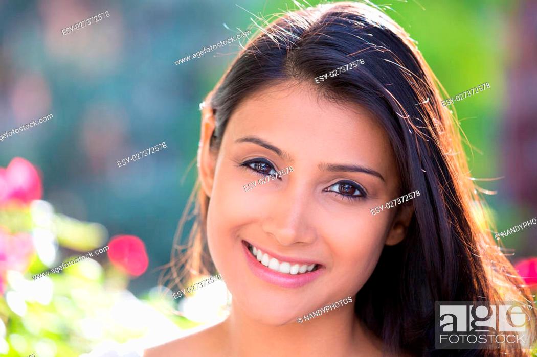 Stock Photo: Closeup headshot portrait of confident smiling happy pretty young woman, isolated background of blurred trees, flowers. Positive human emotion facial expression.