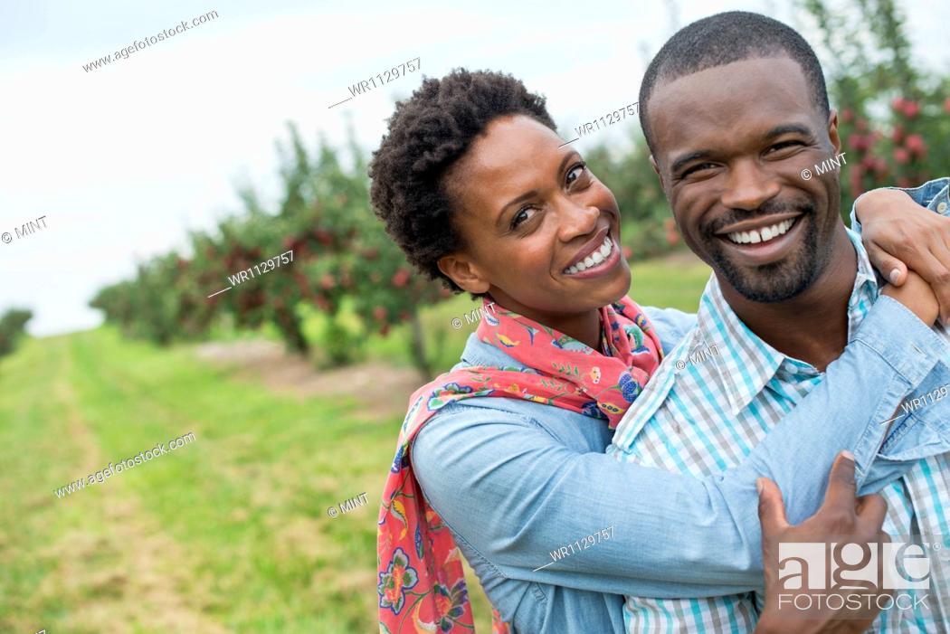 Stock Photo: An organic apple tree orchard. A couple hugging and smiling at the camera.