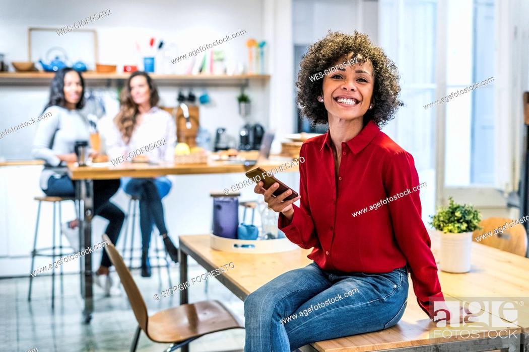 Stock Photo: Portrait of happy woman with cell phone sitting on table.