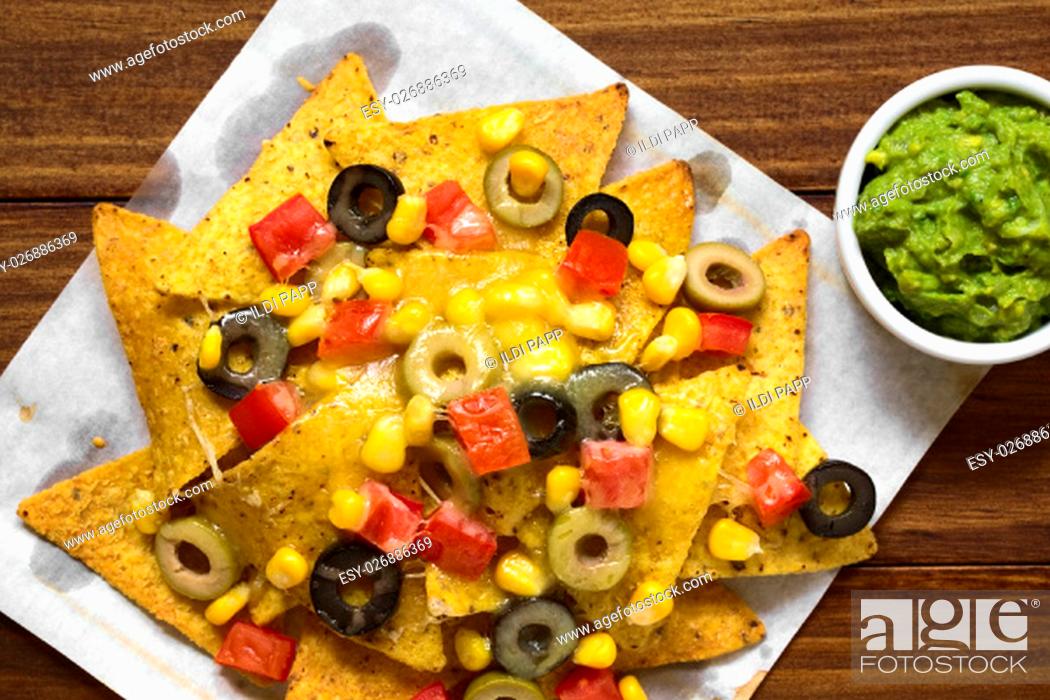 Stock Photo: Baked nachos with cheese, green and black olives, tomato and corn, with guacamole on the side, photographed overhead with natural light (Selective Focus.