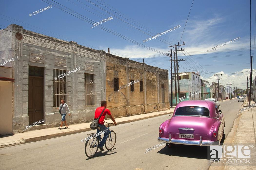 Stock Photo: Cyclist and old American car in front of the colonial buildings at the historic center, Cienfuegos, Cienfuegos Province, Cuba, West Indies, Central America.