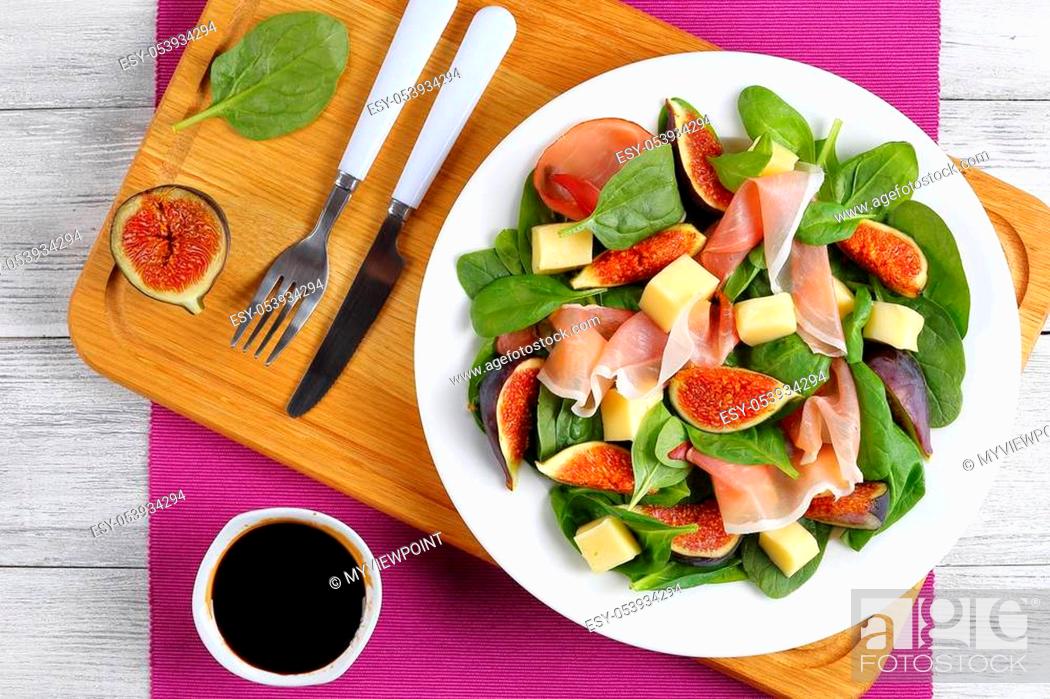 Stock Photo: fresh baby spinach, figs, thinly sliced italian ham and tender mozzarella cheese salad on white plate on cutting board with dressing and cutlery on table mat on.