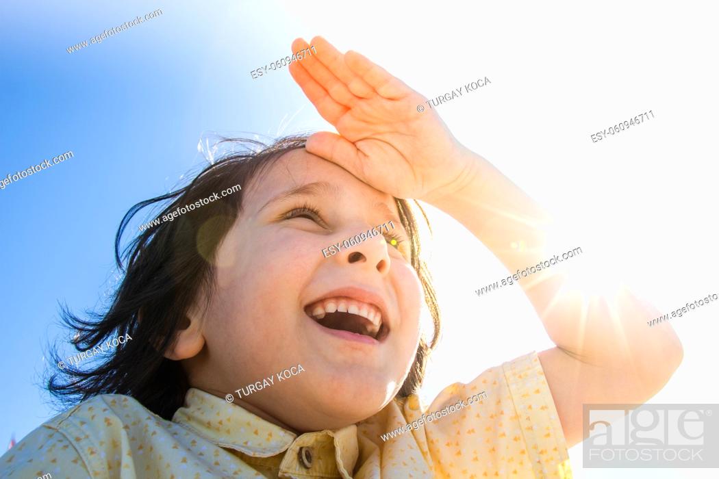 Stock Photo: Happy boy in flare sunshine with hand at forehead.