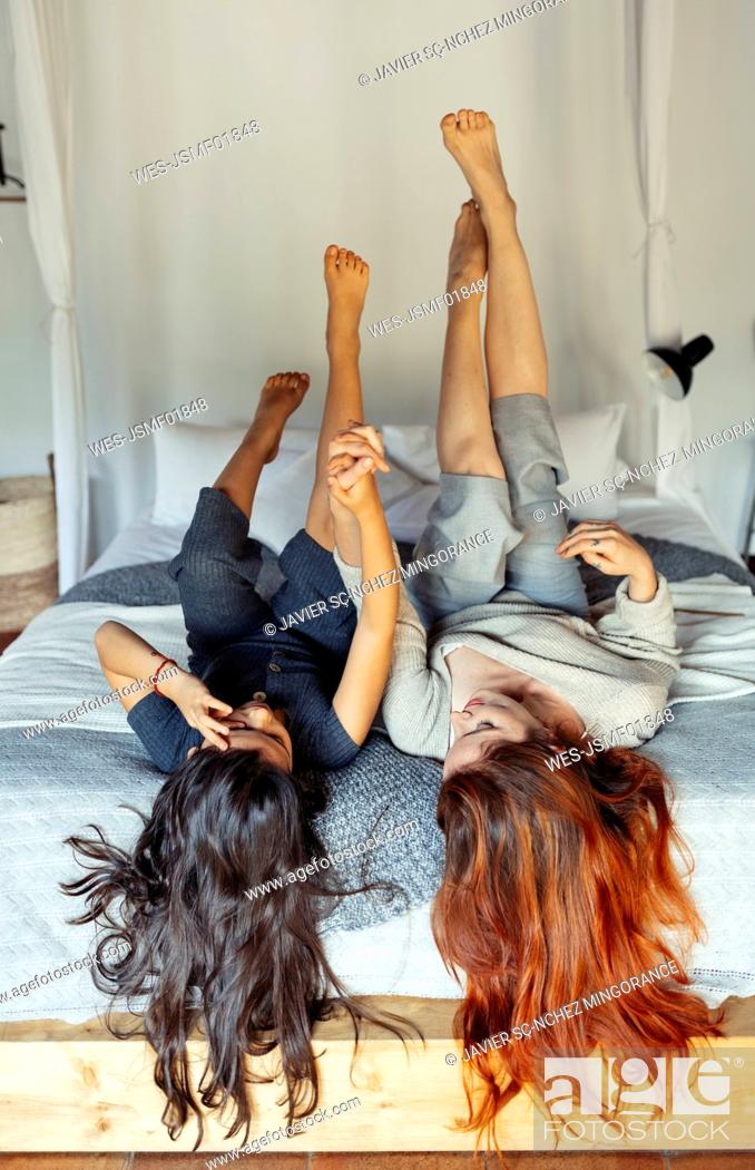 Stock Photo: Girl and redhead woman holding hands while lying on bed at home.