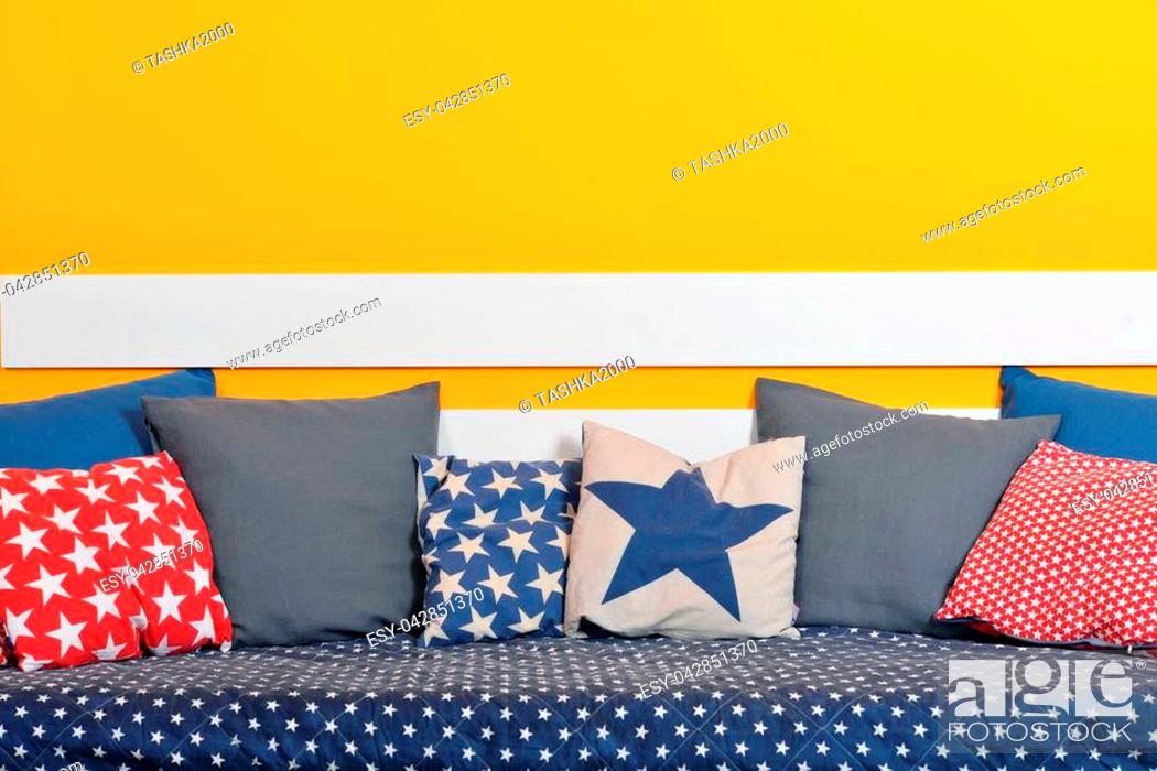 Stock Photo: Children's bed with different color pillows against orange wall in the room.