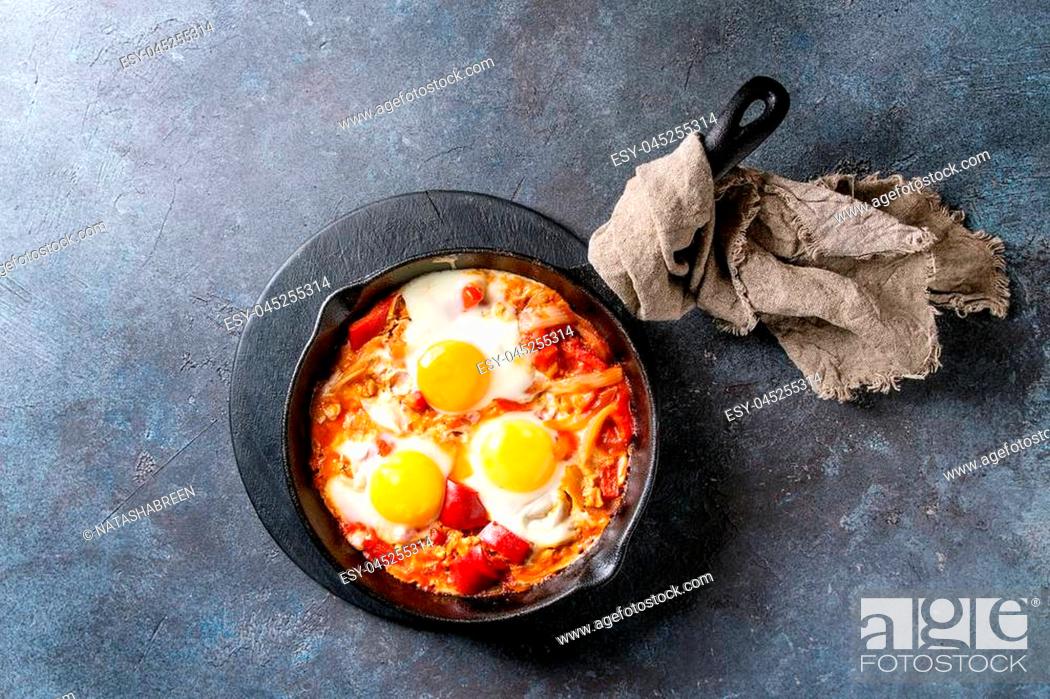 Stock Photo: Traditional Israeli Cuisine dishes Shakshuka. Fried egg with vegetables tomatoes and paprika in cast-iron pan on wooden board with cloth over blue texture.