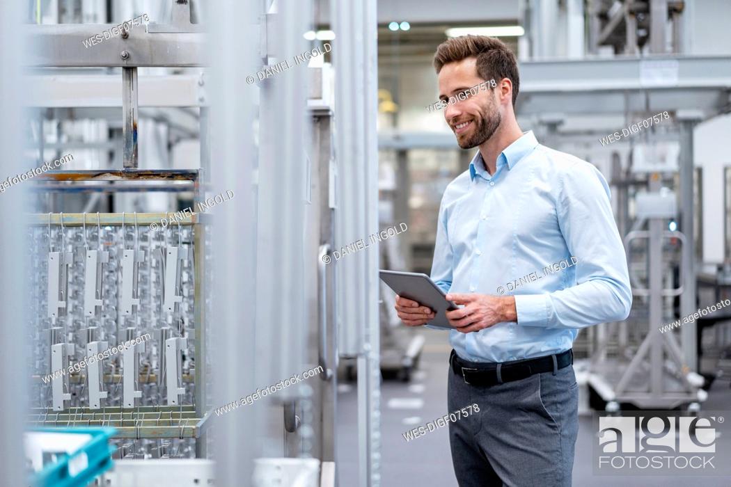 Stock Photo: Smiling businessman with tablet talking in a modern factory.