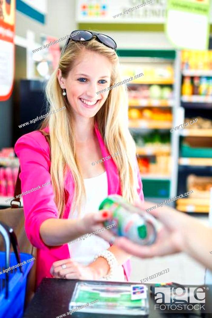 Stock Photo: Beautiful young woman paying for her groceries at the counter of a grocery store/supermarket.