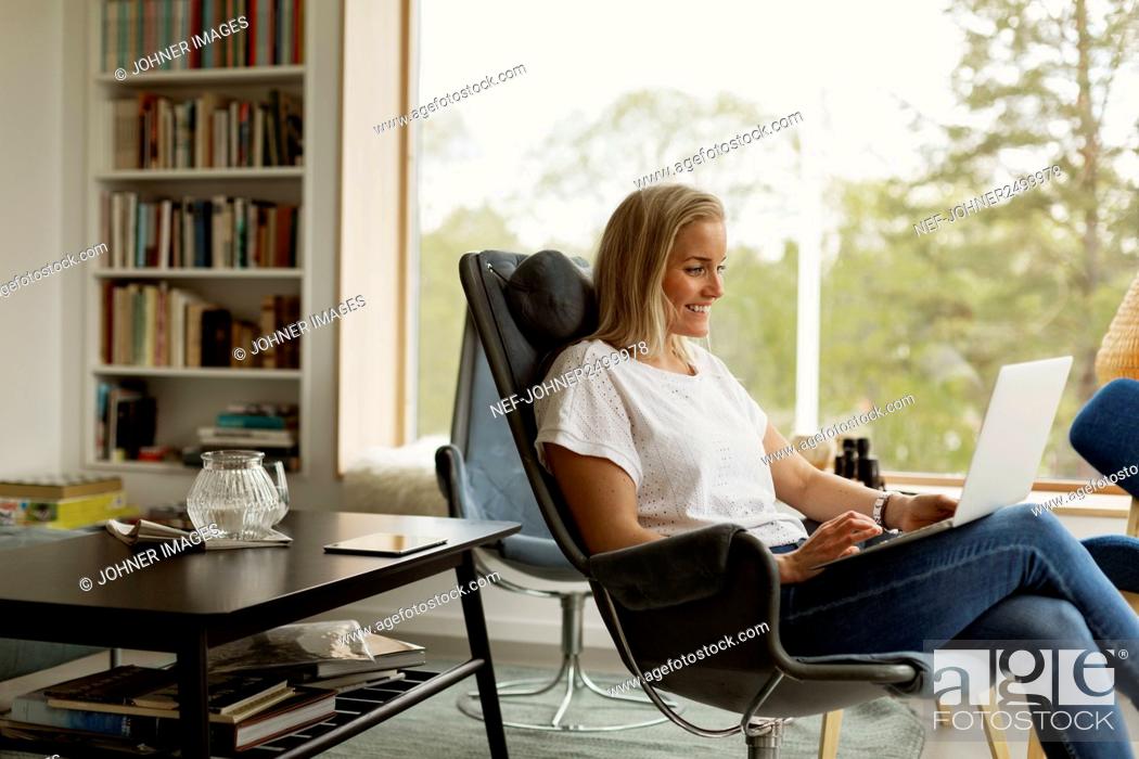 Stock Photo: Woman sitting in living room and using laptop.