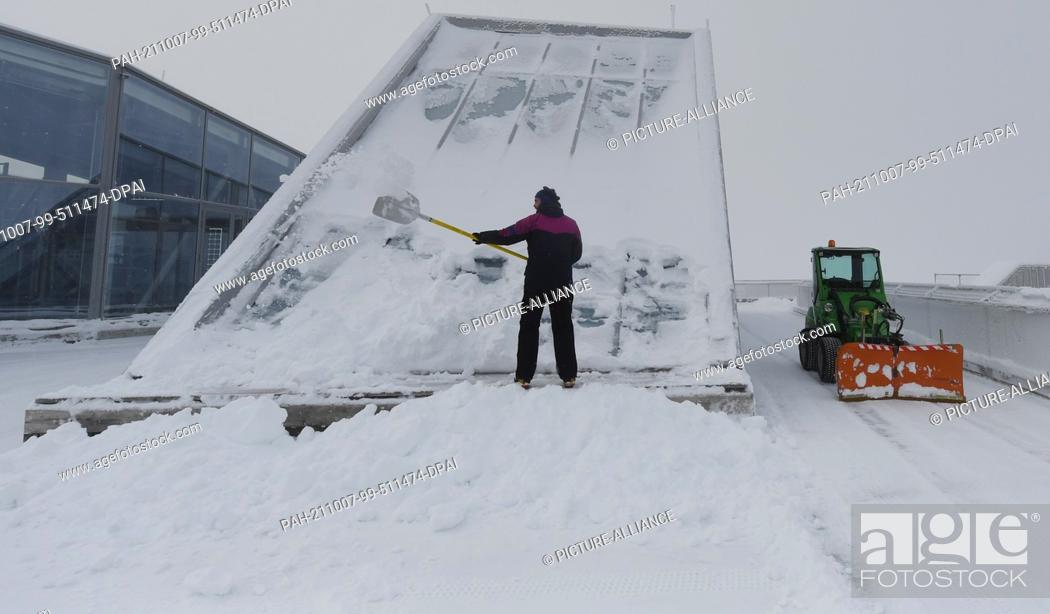 Stock Photo: 07 October 2021, Bavaria, Grainau: An employee clears the roof terrace of the Zugspitze mountain station with a snow shovel.