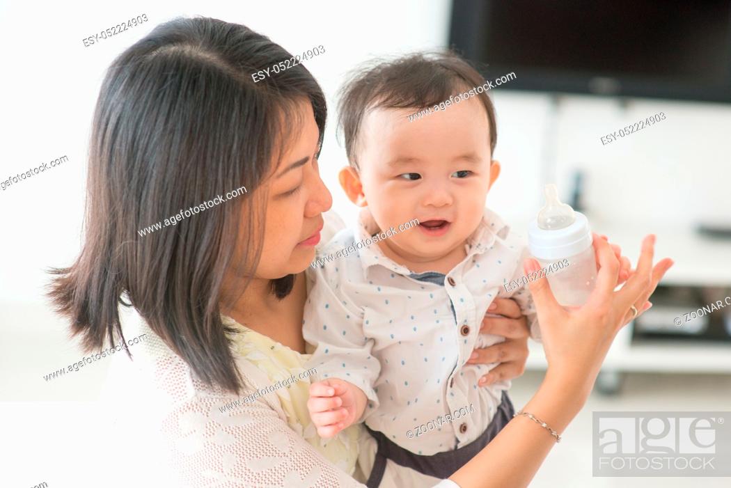 Stock Photo: Mother holding milk bottle with 9 months old child. Asian family at home, living lifestyle indoors.