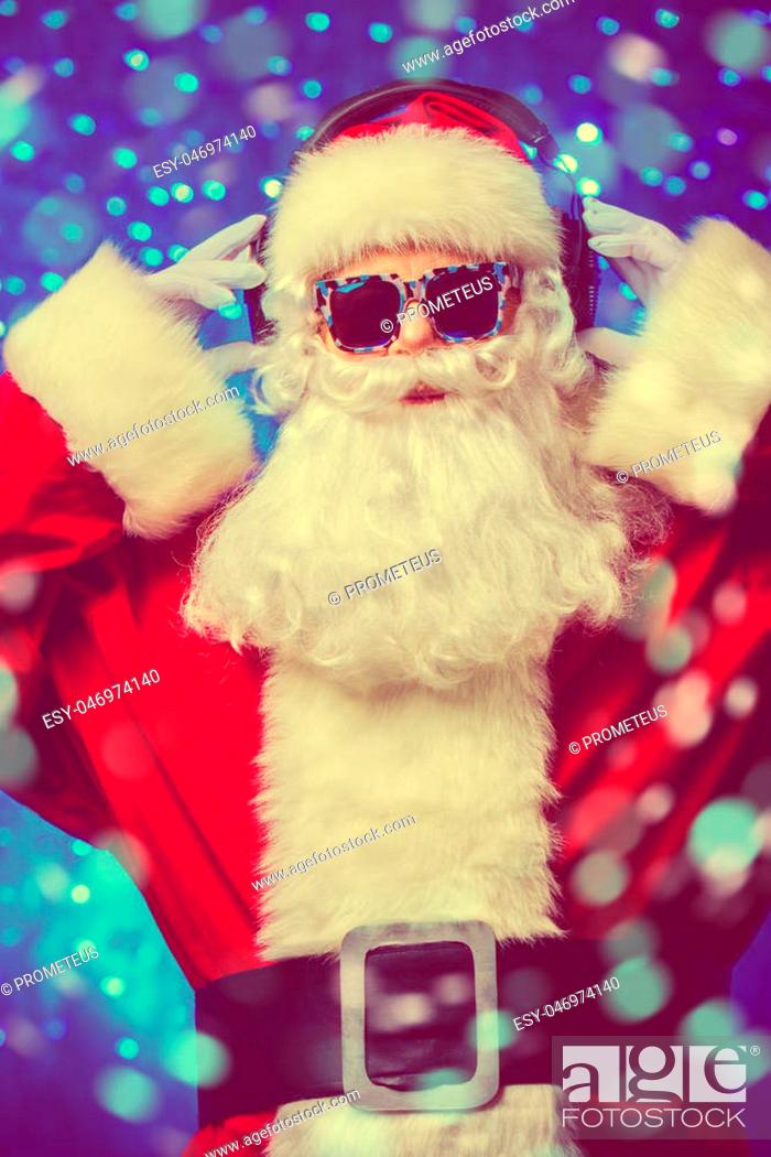 Stock Photo: DJ Santa Claus in sunglasses and headphones. Christmas songs and music. Disco lights in the background.