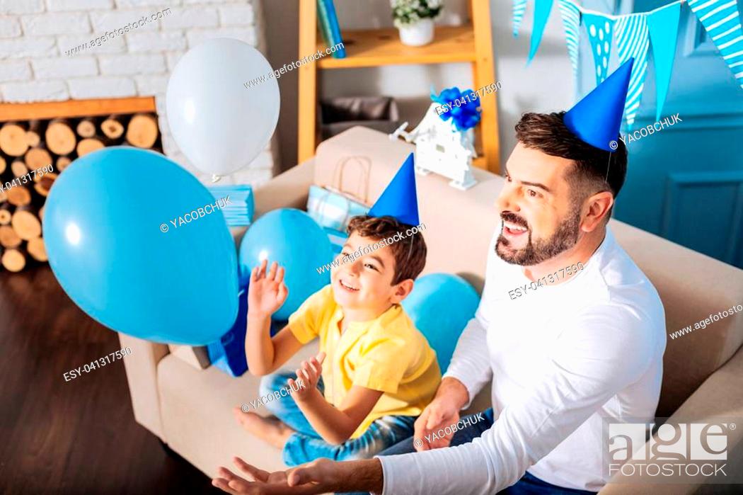 Imagen: Funny game. Adorable little boy and his upbeat father sitting on the sofa and playing with balloons during the birthday party of the kid.