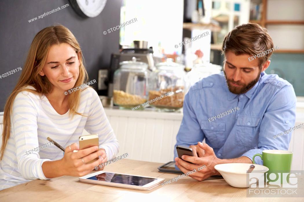 Stock Photo: Young Couple Eating Breakfast Whilst Using Mobile Phones.