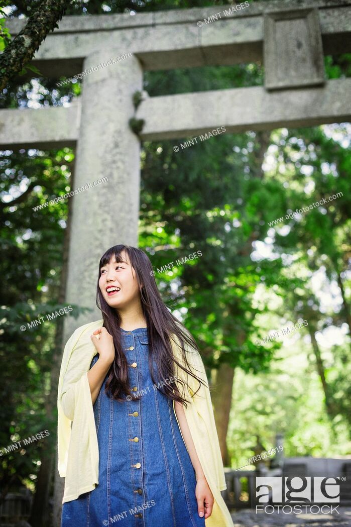 Stock Photo: Smiling young woman wearing blue dress and yellow shirt at Shinto Sakurai Shrine, Fukuoka, Japan.