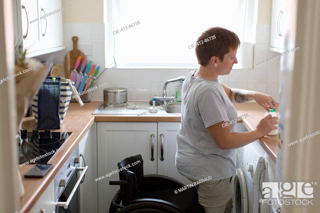 Stock Photo: Young woman with wheelchair in apartment kitchen.