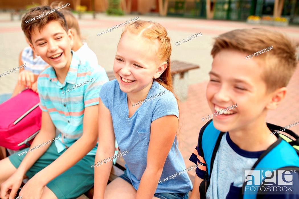 Stock Photo: primary education, friendship, childhood, communication and people concept - group of happy elementary school students with backpacks sitting on bench and.